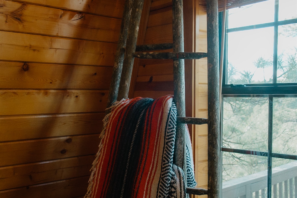Rustic A-frame charm meets mountain views with this cozy ladder nook and natural wood interior. Sunlight pours in through the window, highlighting the cabin’s warm, inviting design in Arizona’s White Mountains.