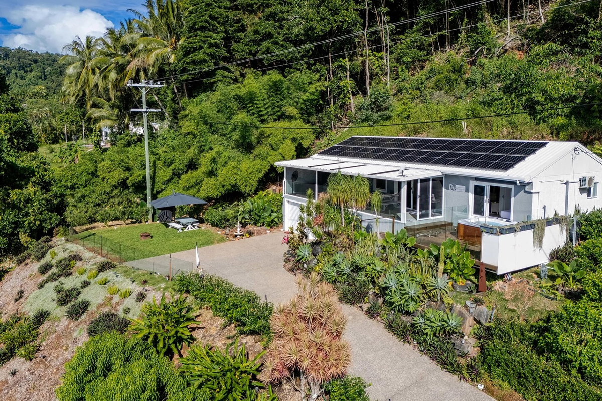 The home’s exterior shows the private driveway, landscaped gardens, covered entry and solar panels, with the spa deck tucked along the side.