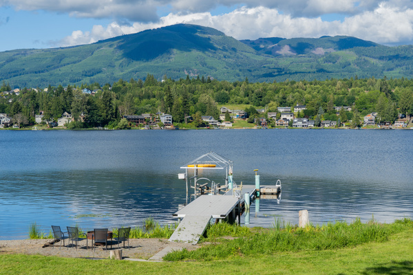 A dock stretches into the calm lake, accessible by a pathway with sand on one side and grass on the other. It’s perfect for mooring a boat or sitting by the water, blending natural textures with the peaceful lakeside setting.