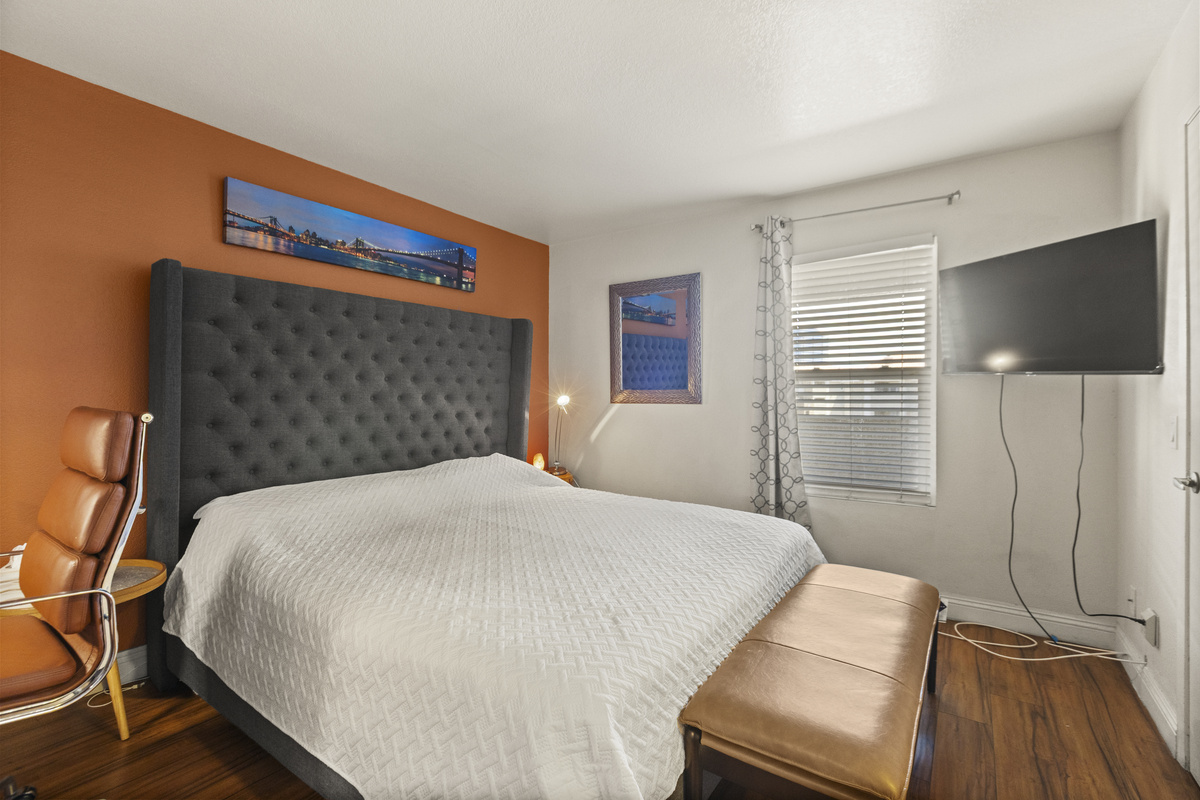 Bedroom 1 with king bed, wall-mounted TV, desk chair, and full bathroom access nearby.
