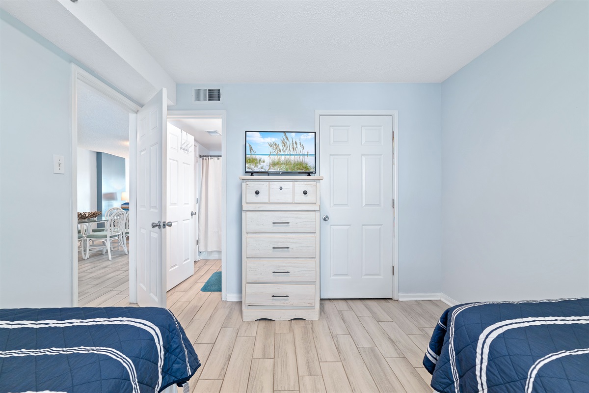 A charming Twin bedroom featuring an ensuite bathroom, flat-screen TV and dresser, perfect for sharing and relaxation after a day of coastal adventures.