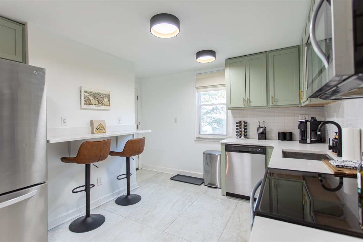 Modern kitchen with stainless steel appliances, coffee station, and a breakfast bar with seating for two.