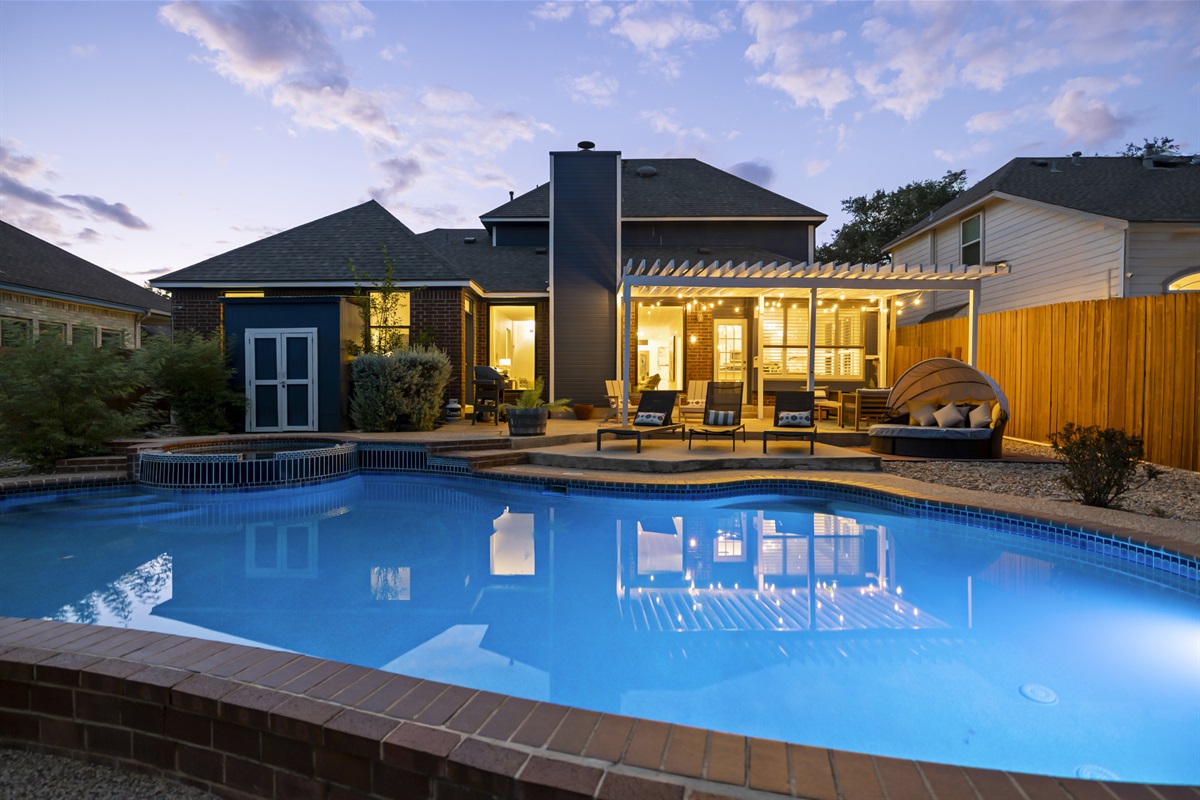 Stunning backyard retreat featuring a sparkling pool, spa, and a covered patio with cozy seating and string lights. Perfect for relaxing evenings or outdoor entertaining.