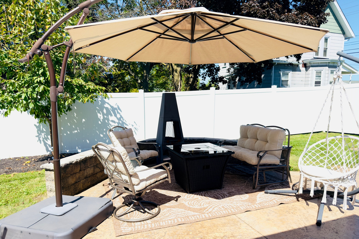 Back patio with cushioned seating, dining space, an umbrella, and a gas firepit.
