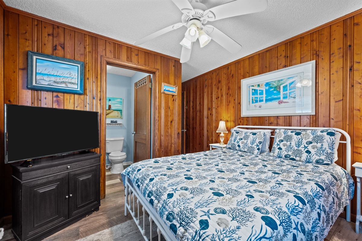 Large Smart TV, cozy decor, and stunning wood paneling in master bedroom