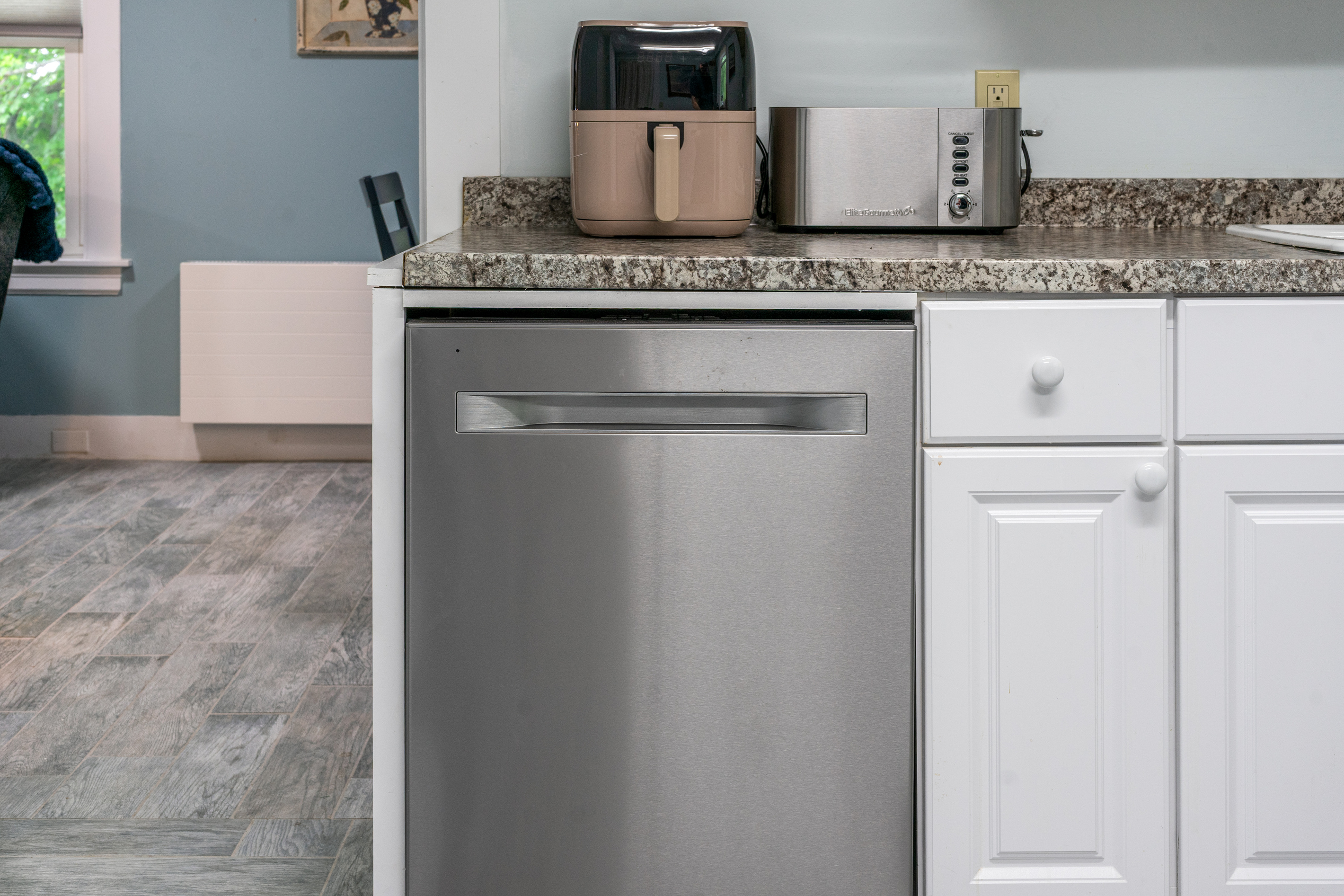 This fully equipped kitchen setup includes a stainless steel dishwasher, a multi-slice Elite Gourmet toaster, and a convenient air fryer. Positioned near the dining archway, this layout optimizes mealtime cleanup for your Maine vacation.