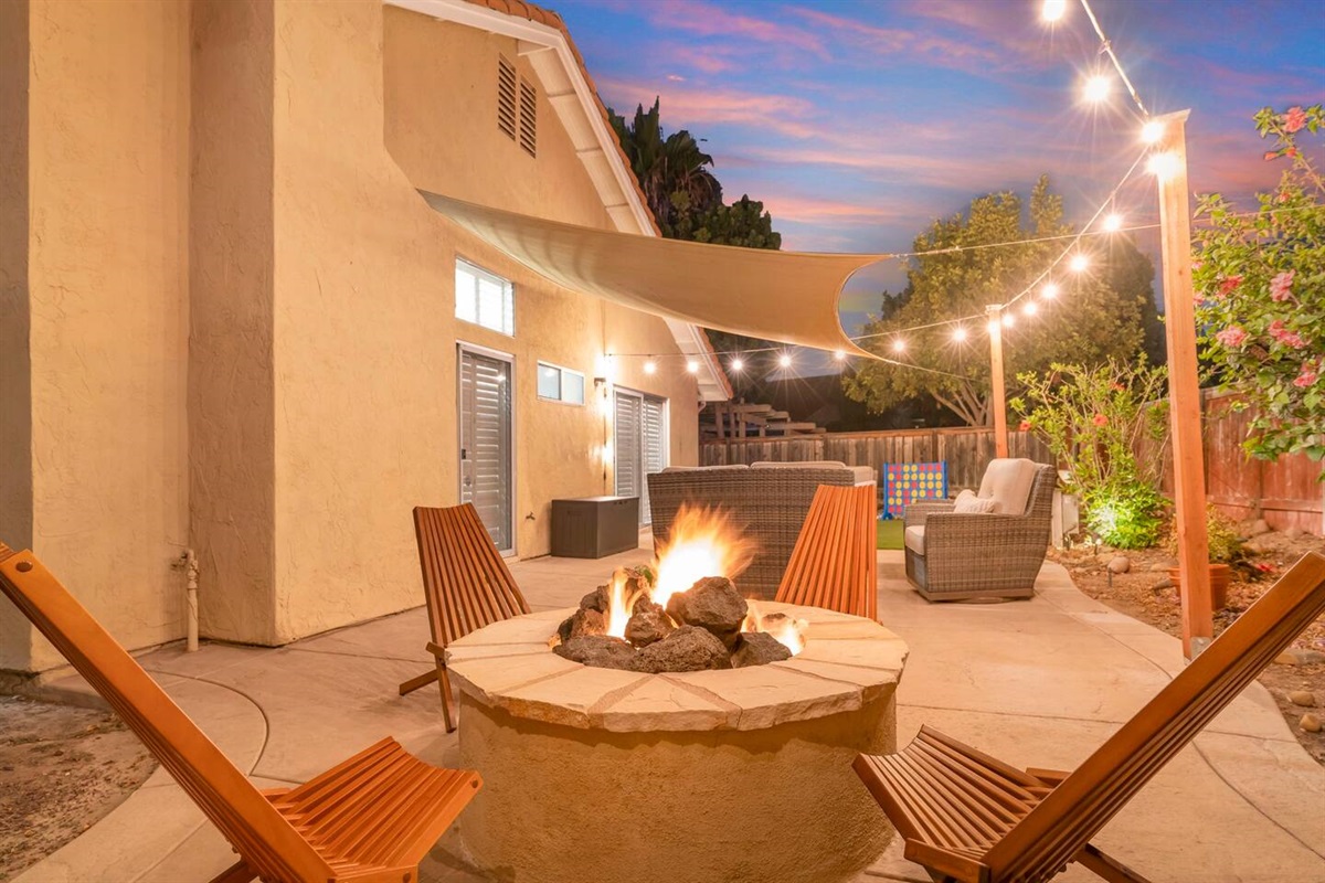 The fully fenced corner lot backyard is a charming retreat with a landscaped garden, a cozy fire pit, and a patio set for gatherings. Twinkling patio lights and a sunshade sail add ambiance and comfort, making it perfect for outdoor relaxation.