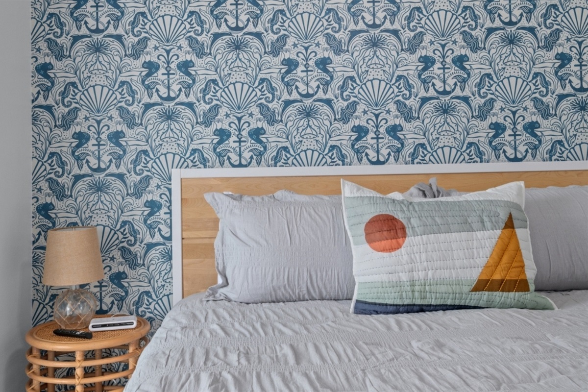 Whimsical seahorse wallpaper and a king bed dressed in soft coastal tones.