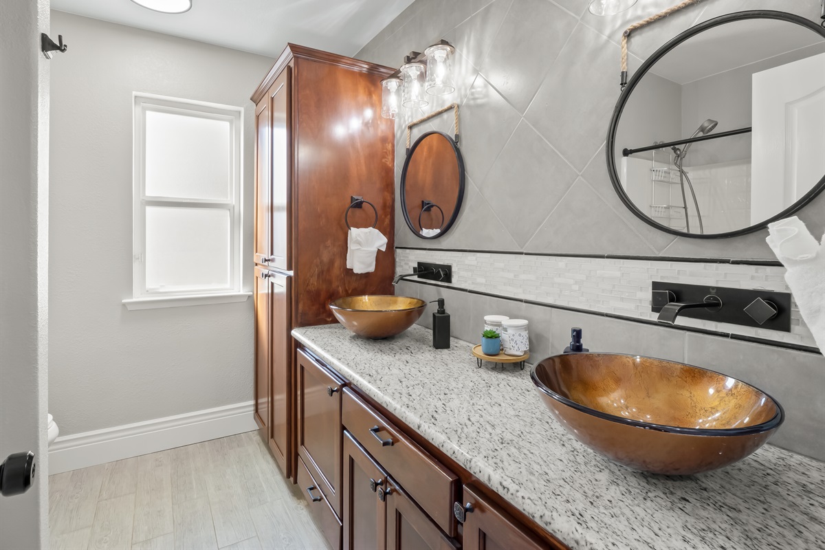 Elegant spa-style bathroom featuring dual vessel sinks, rich wood cabinetry, granite counters, and designer lighting—an elevated space designed for comfort and style.