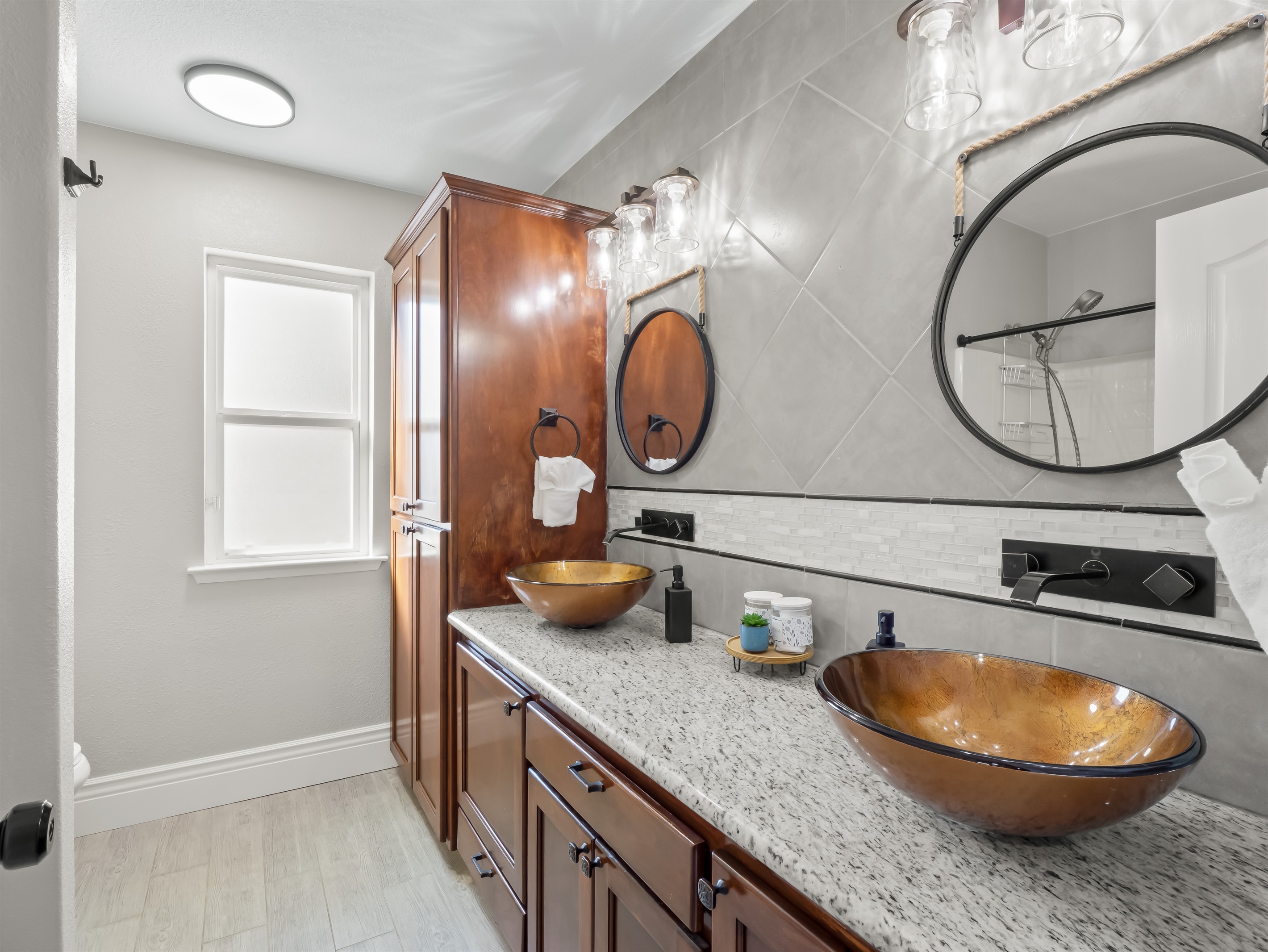 Elegant spa-style bathroom featuring dual vessel sinks, rich wood cabinetry, granite counters, and designer lighting—an elevated space designed for comfort and style.