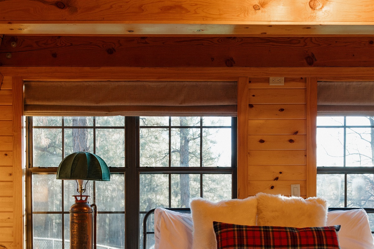 The cozy bedroom at Poppywood Pines features plush bedding with tartan accents and forest views. This gothic western Show Low A-frame offers comfortable accommodations for restful nights, perfect after exploring White Mountains hiking trails, fishing, and