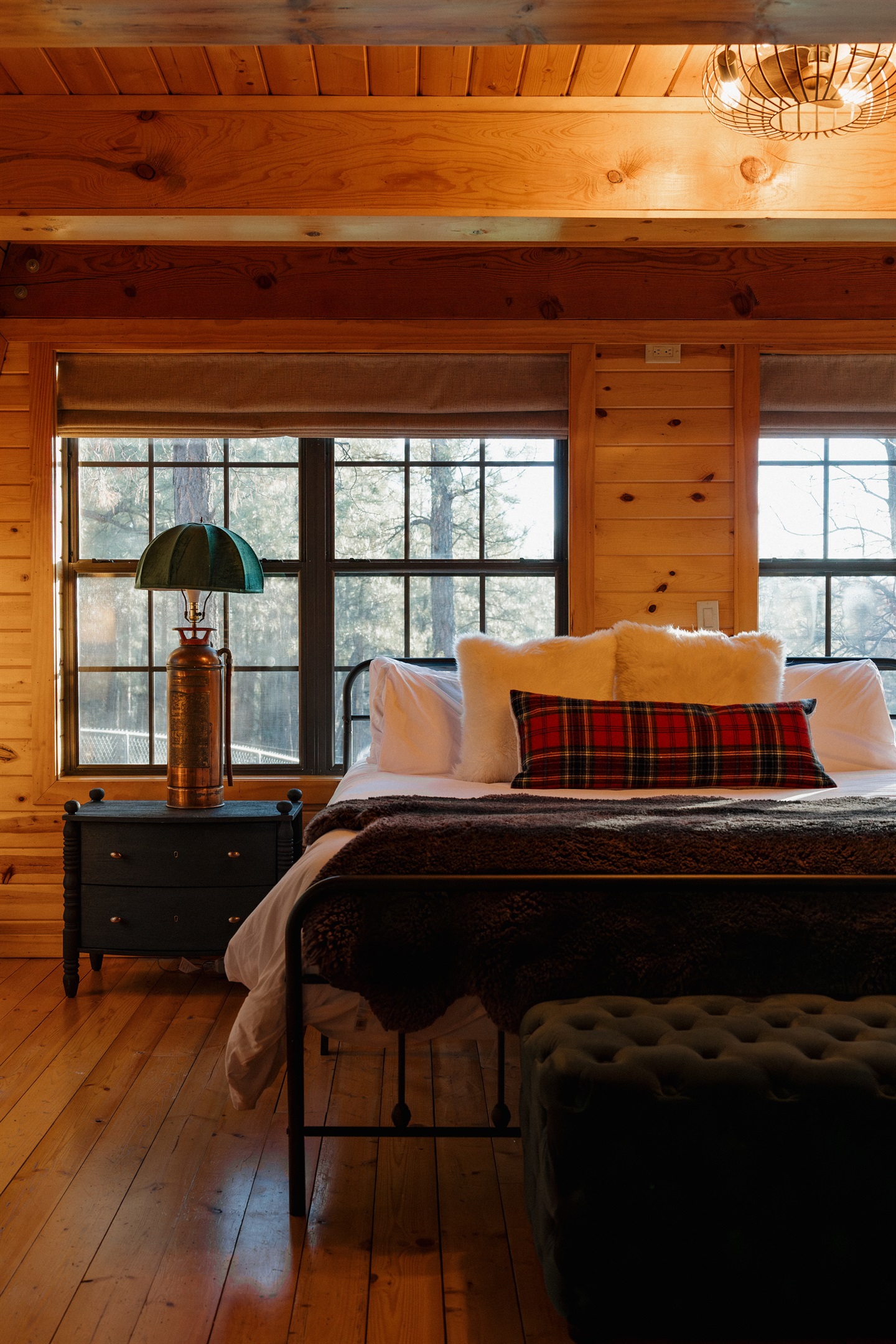 The cozy bedroom at Poppywood Pines features plush bedding with tartan accents and forest views. This gothic western Show Low A-frame offers comfortable accommodations for restful nights, perfect after exploring White Mountains hiking trails, fishing, and