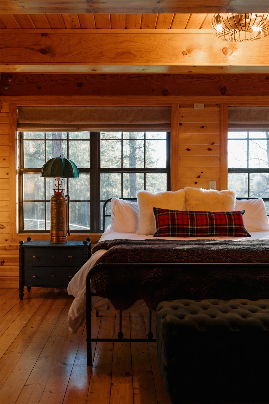 The cozy bedroom at Poppywood Pines features plush bedding with tartan accents and forest views. This gothic western Show Low A-frame offers comfortable accommodations for restful nights, perfect after exploring White Mountains hiking trails, fishing, and