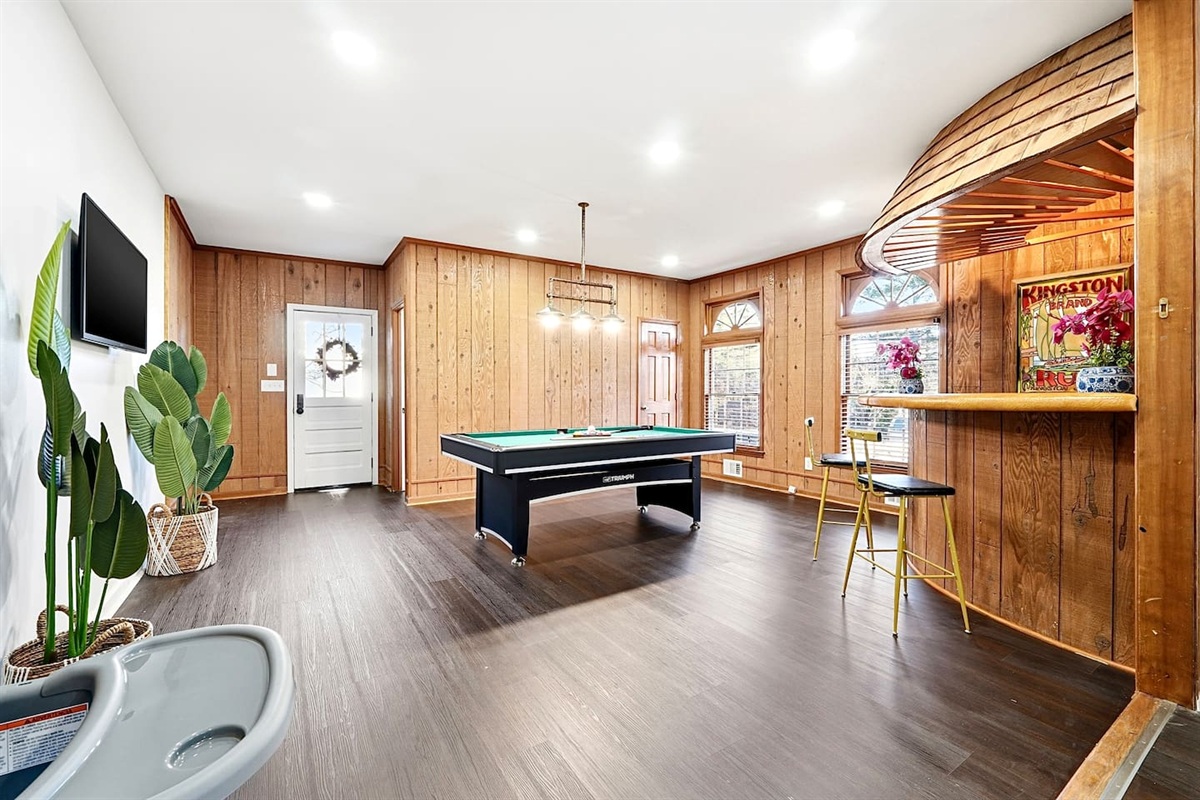 Enjoy this main-floor game room near the side entrance featuring a convertible pool and ping-pong table, a custom curved wood bar, and a Roku powered smart TV—ideal for entertaining and casual gatherings.