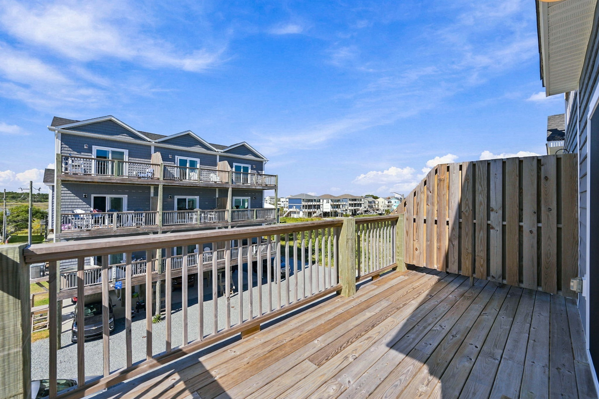 Spacious private wooden balcony featuring railing for safety, a vertical wooden privacy partition, and sunny views overlooking the coastal resort community.  