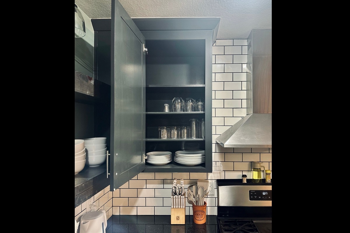 Kitchen cabinet stocked with drinking glasses, wine glasses, bowls, and plates for comfortable dining at home.