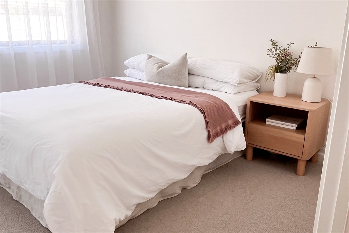 The queen bed has layered pillows, white linen and bedside lighting, giving this room a simple, comfortable setup.