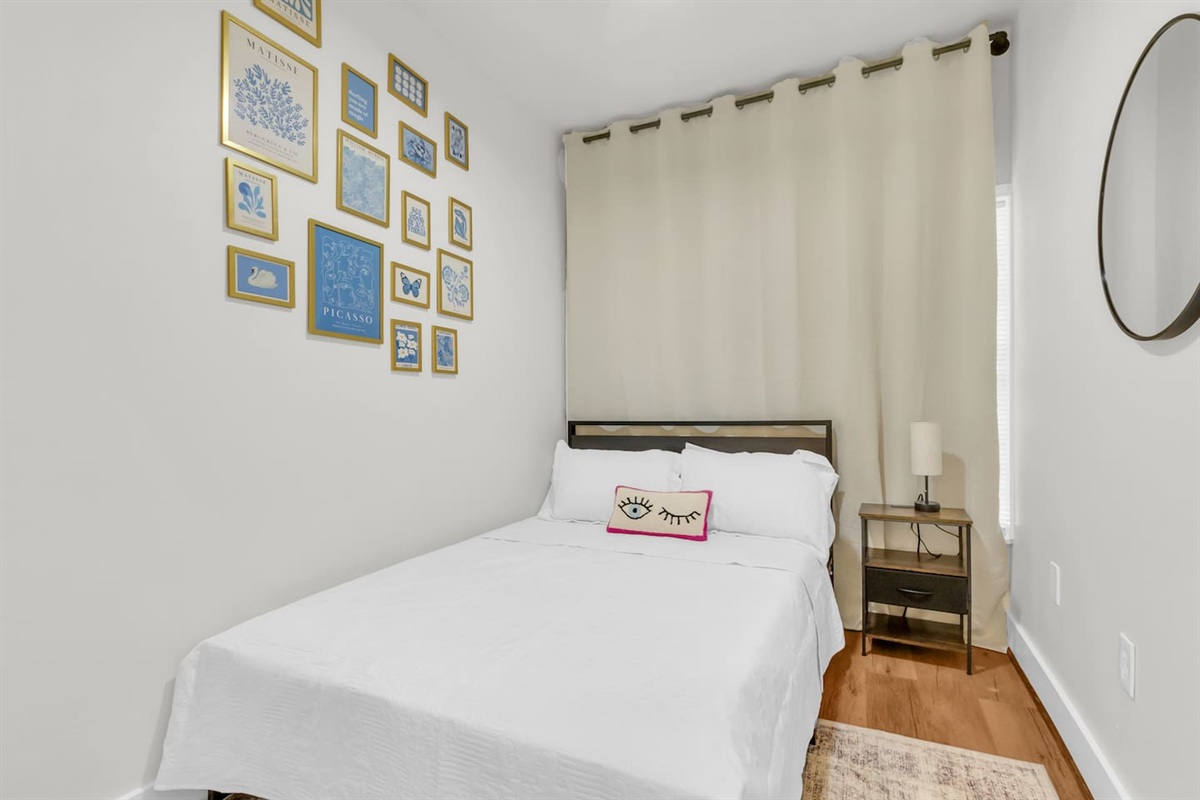 Bedroom with full bed, mirror, room darkening shades, and colorful artwork accents.