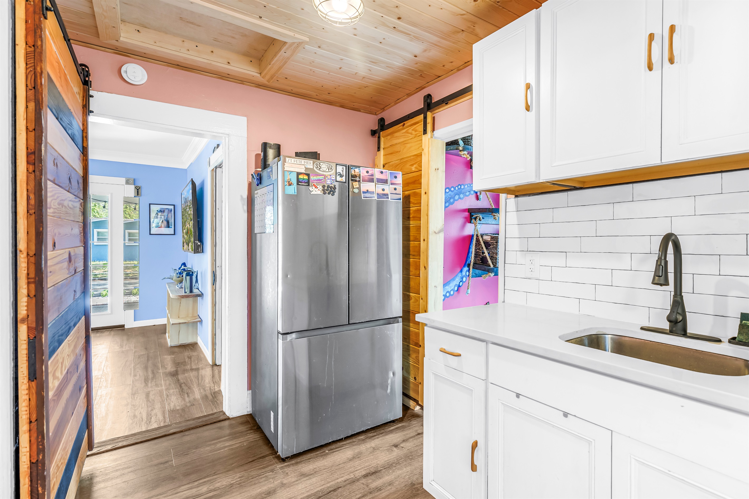 Bright kitchen area with white cabinetry, stainless steel refrigerator, wood ceiling accents, and easy access to the rest of the home.