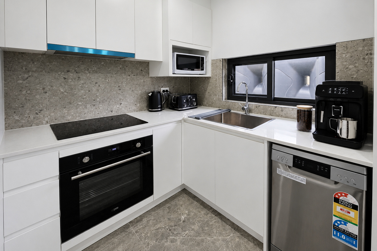 Matilda’s Urban Escape includes a compact kitchen with white cabinetry, grey tiled splashback and a window above the sink.