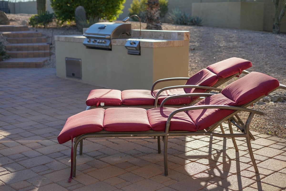 Comfortable red loungers positioned near the BBQ area for laid-back afternoons in the sun.
