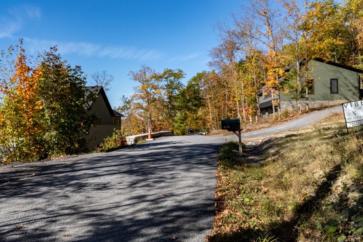 Gravel driveway view leading to cabin with lake-view in background.