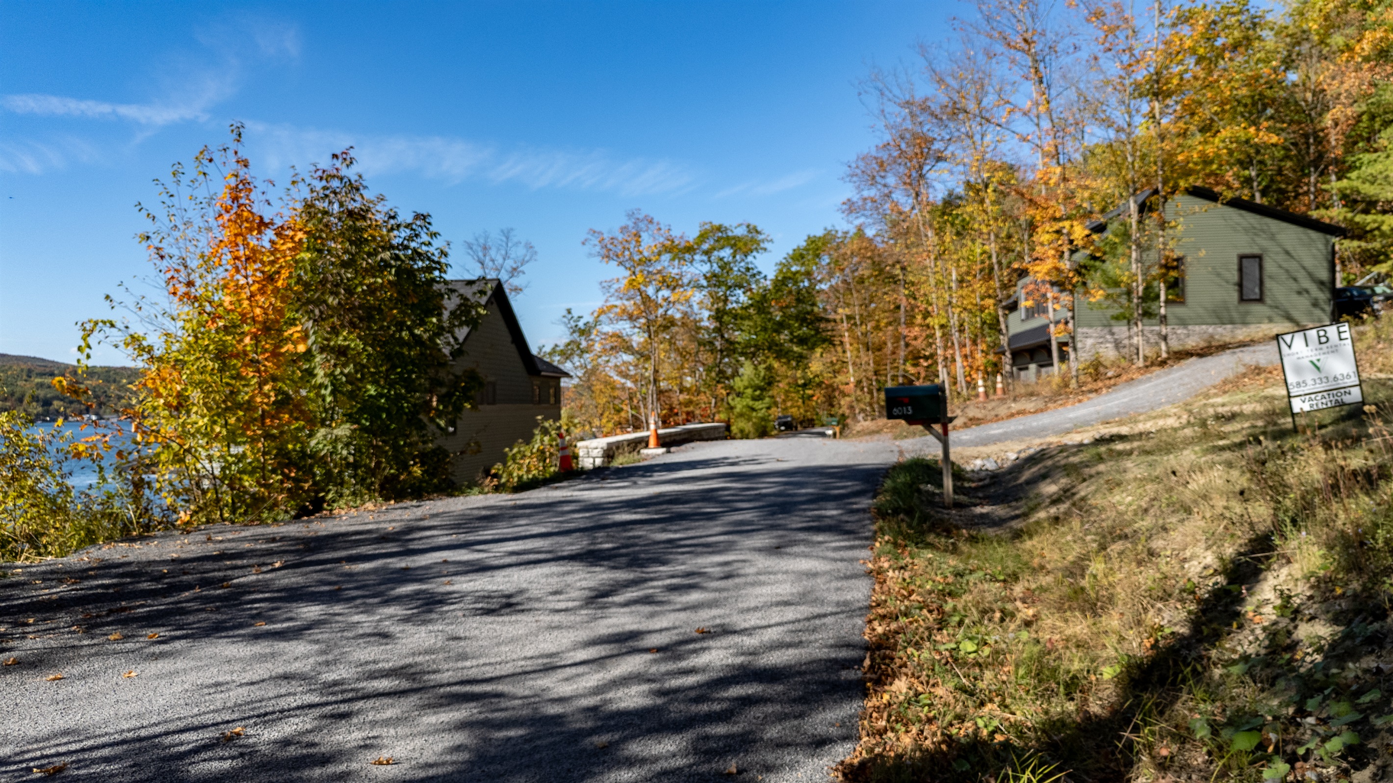 Gravel driveway view leading to cabin with lake-view in background.
