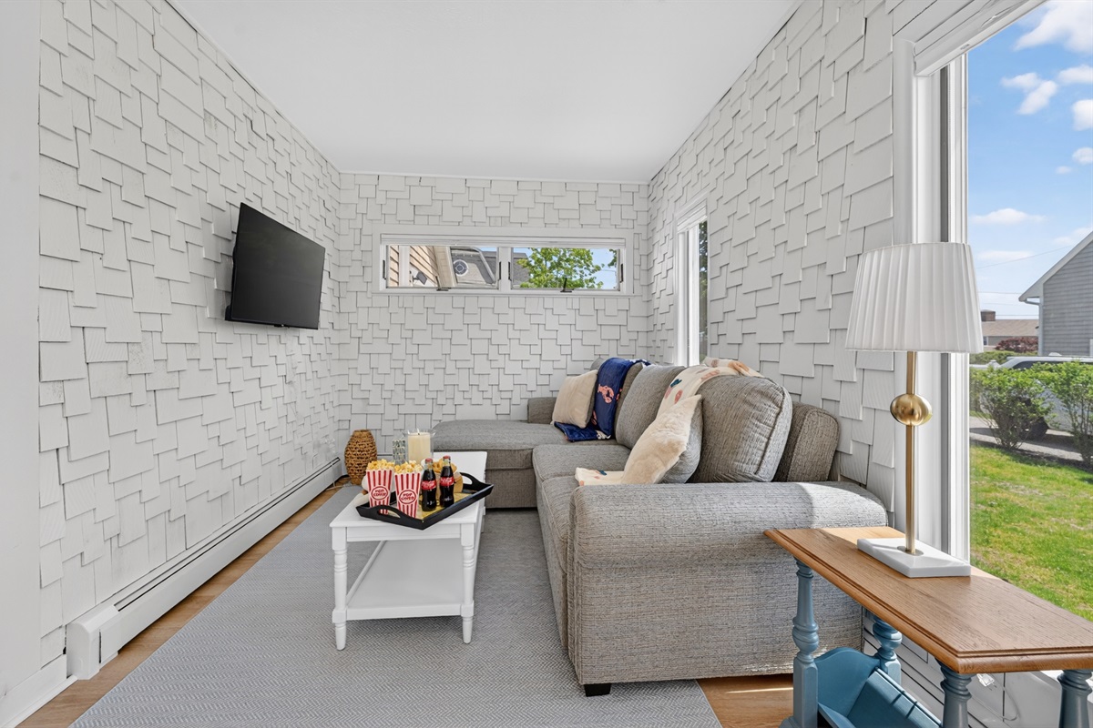 Cozy entertainment-ready living room with wide windows, warm natural light, and a comfortable seating arrangement for movies, games, or downtime.