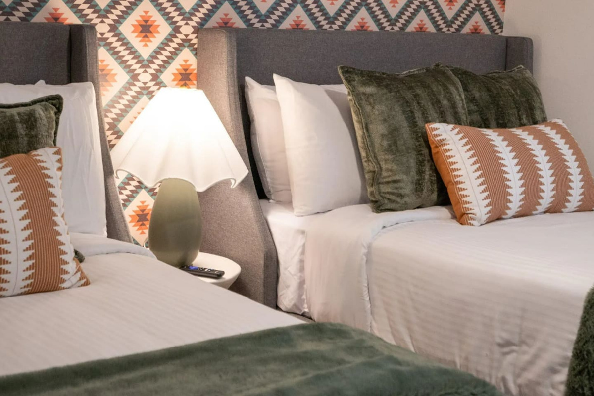 Two beds dressed in plush layered linens, set against a bold Southwest print — a room designed for kids, friends, or anyone who wants their own space.