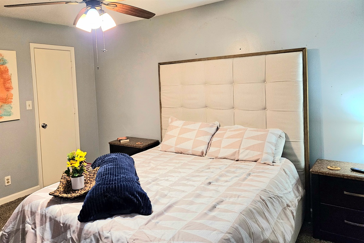 Queen primary bedroom with extra seating, ceiling fan, fast WIFI, TV, ensuite bathroom, and walk-in closet. Big window overlooking the fenced back yard adds fresh natural light and appeal.