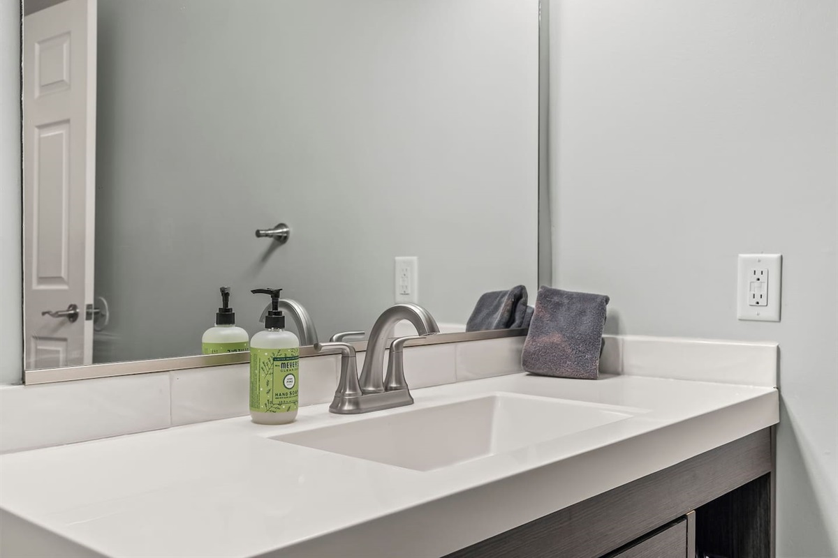 Close-up of the sink and vanity featuring a modern faucet, clean countertop, and provided hand soap.