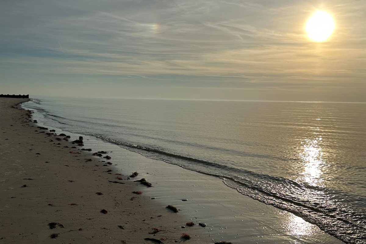 A serene and tranquil beach scene, where the sun reflects beautifully across the gentle, calm ocean waves. It is an ideal setting for enjoying a peaceful moment by the water.
