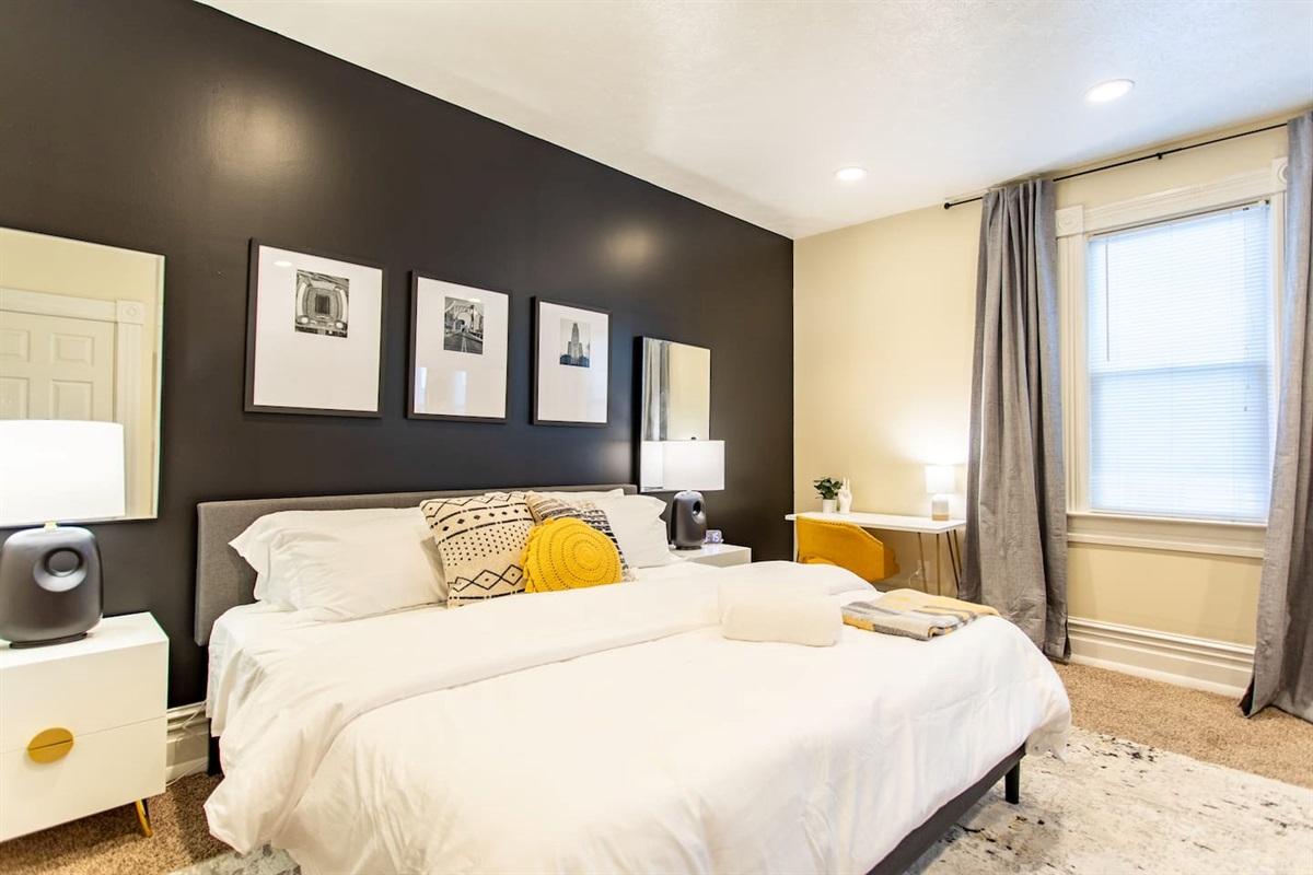 A cozy king-sized bed with soft, inviting linens, positioned beside a large window that lets in natural light, offering a peaceful and serene atmosphere.