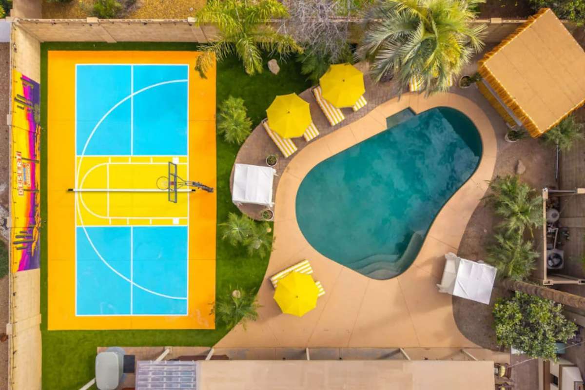 Overhead view of pool and sports court with yellow umbrellas and green landscaping—compact yet complete recreation space for guests.
