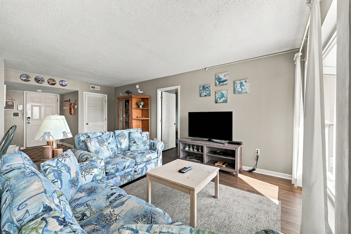Bright living area with a pull-out sofa, flat-screen TV, coffee table, and balcony access.