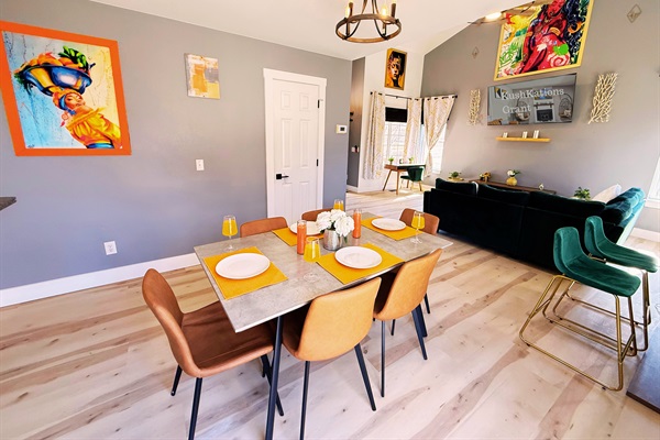 A stylish and inviting dining area with a modern table, sleek leather chairs, vibrant decor, and a chic chandelier—perfect for gatherings and memorable meals