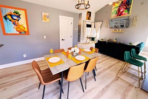 A stylish and inviting dining area with a modern table, sleek leather chairs, vibrant decor, and a chic chandelier—perfect for gatherings and memorable meals