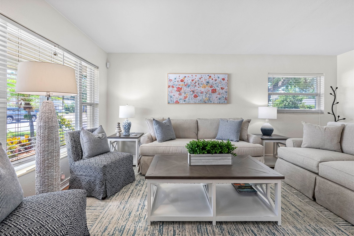 The room features two oversized, cloud-like sofas, a textured armchair with oversized cushions, and two woven poufs—offering plenty of space for families and groups to gather.