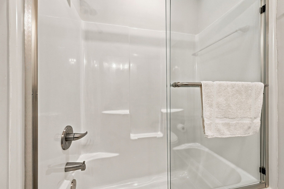 Close-up view of the walk-in tub and shower combination featuring sliding glass doors with a brushed nickel towel bar, sleek metallic fixtures, and built-in shelving inserts.   