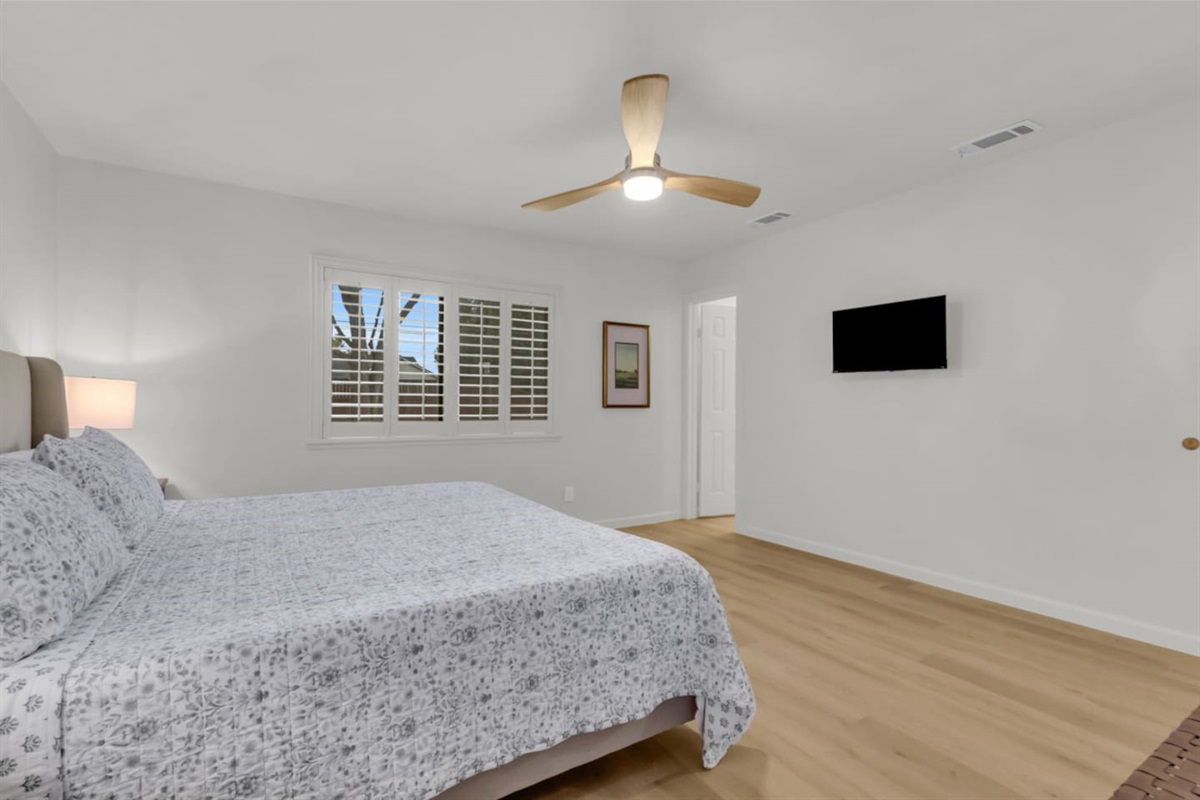 Modern primary suite featuring a mounted TV, ample floor space, and a bright window view. Stay cool with air conditioning and a sleek ceiling fan.