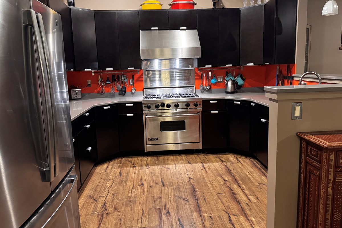 Fully stocked gourmet kitchen featuring a professional Viking range and modern black cabinetry with a bold orange backsplash. Enjoy expansive granite countertops and stainless steel appliances, perfect for preparing meals after a day in Acadia.