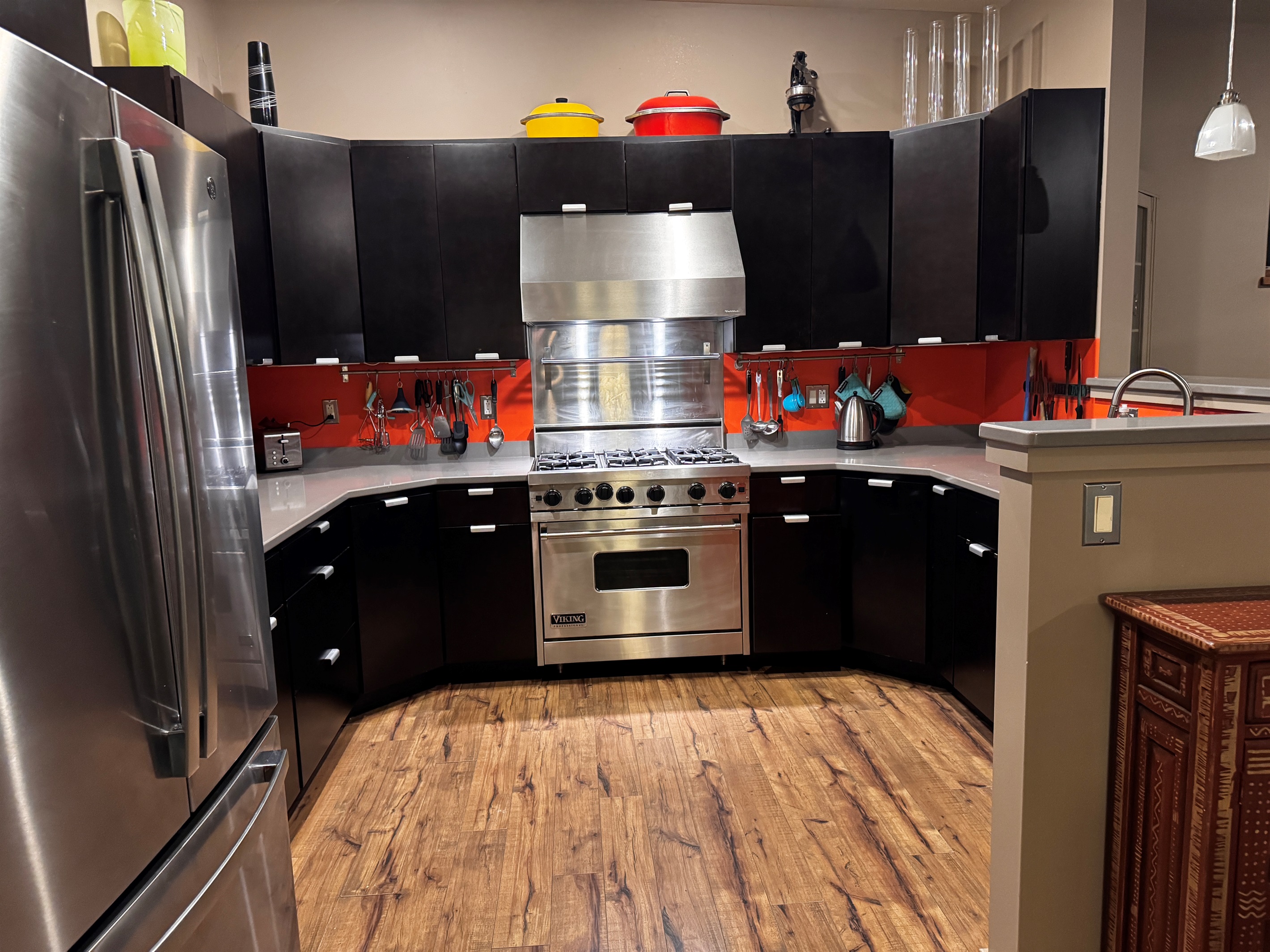 Fully stocked gourmet kitchen featuring a professional Viking range and modern black cabinetry with a bold orange backsplash. Enjoy expansive granite countertops and stainless steel appliances, perfect for preparing meals after a day in Acadia.