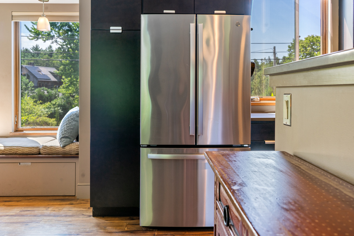 Bright kitchen entrance on the main level featuring a stainless steel refrigerator and modern cabinetry. A sun-filled built-in window seat offers a cozy nook to read or watch life in the historic village of Otter Creek.