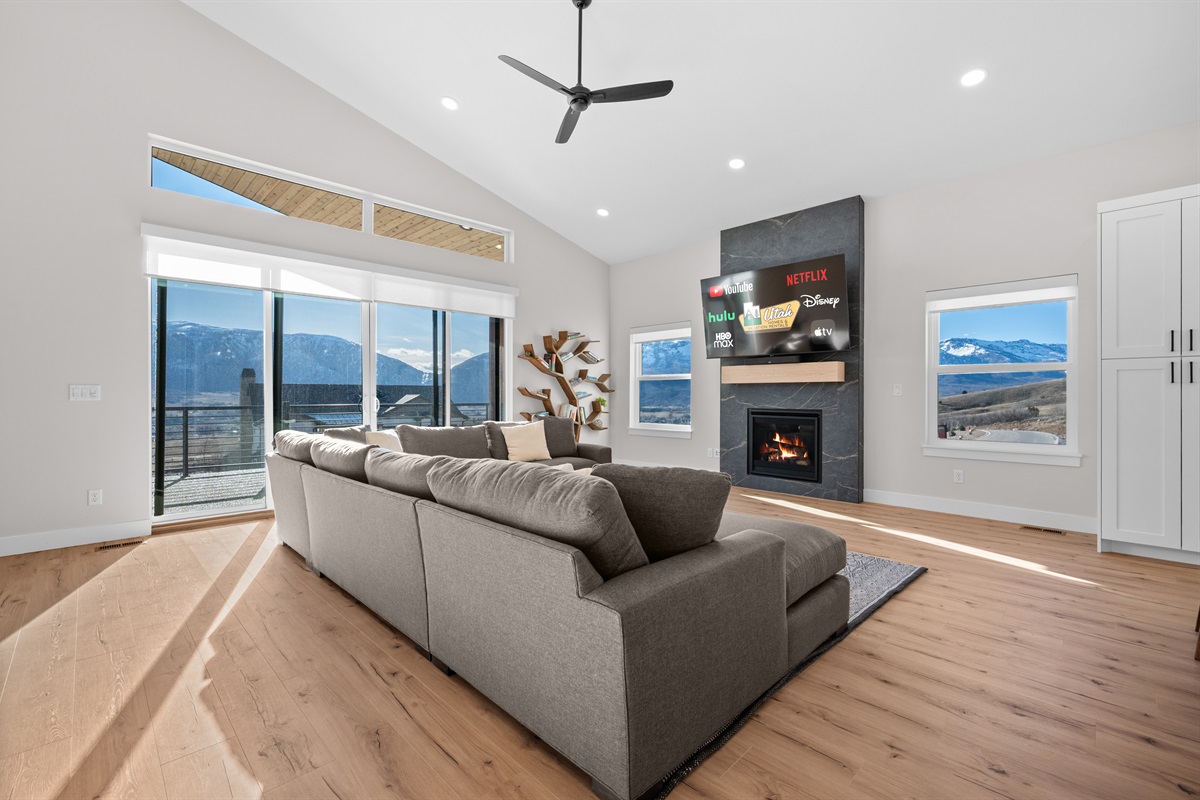 Living room bathed in natural light with a fireplace as centerpiece and surrounding mountain vistas.