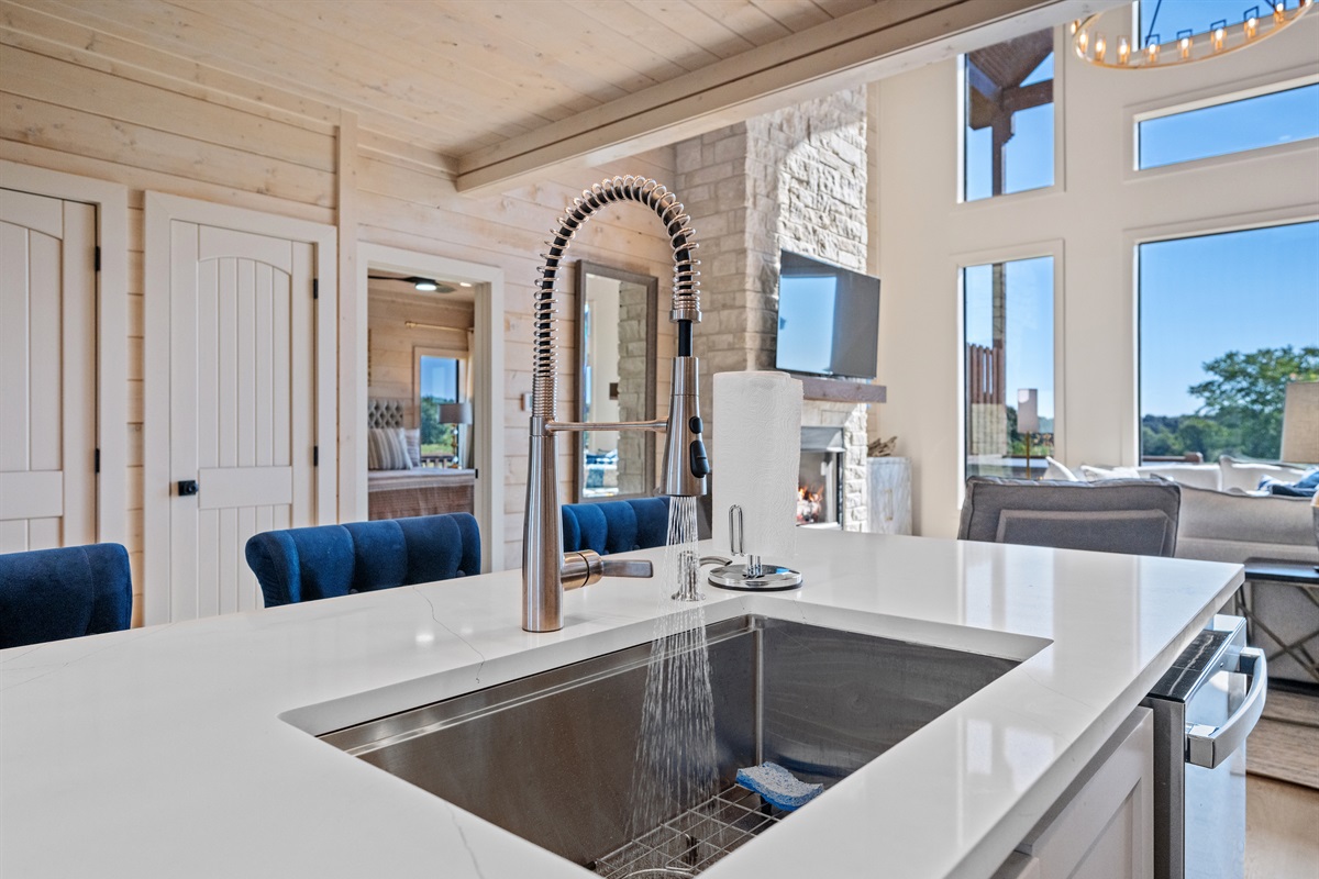 Sleek farmhouse sink and spacious counters overlooking the living area with large windows.