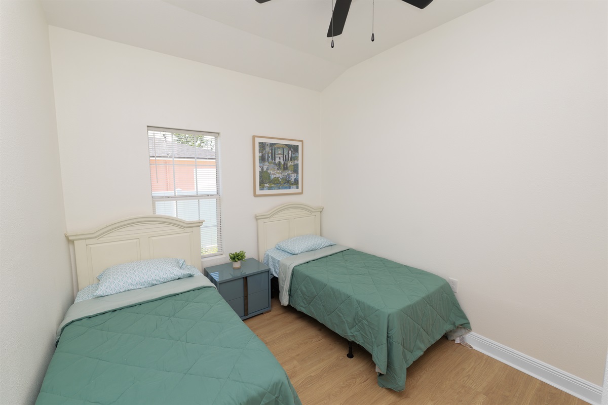 A cheerful and functional setup with twin beds, light wood flooring, and a window view to let in morning sunshine.