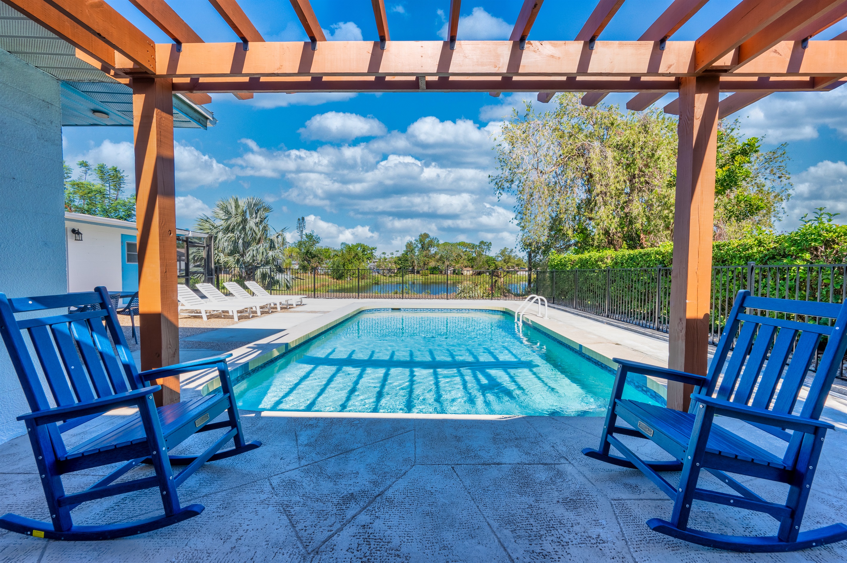 Outdoor Oasis: Relax in rocking chairs overlooking the sparkling pool and serene landscape!