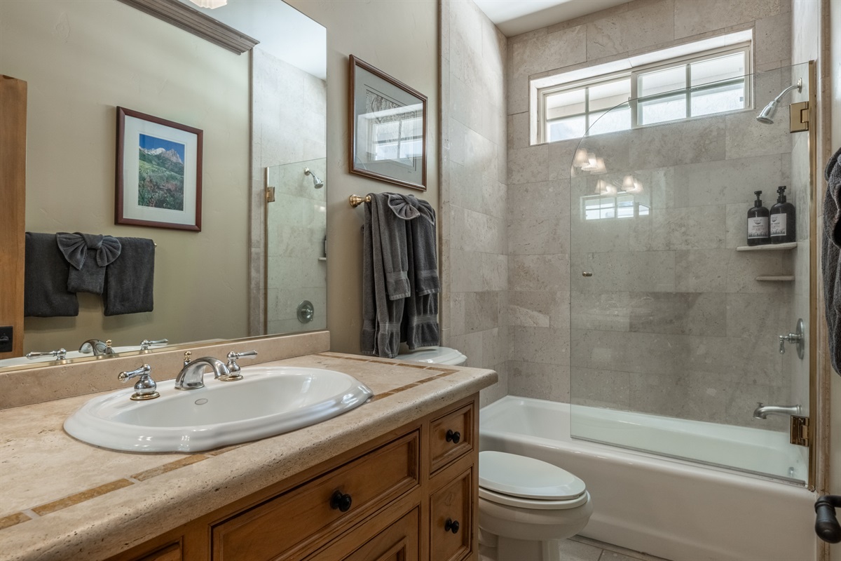 The Charming Chalet hall bath features tub/shower combination tiled in natural stone, and warm-mountain inspired woods.