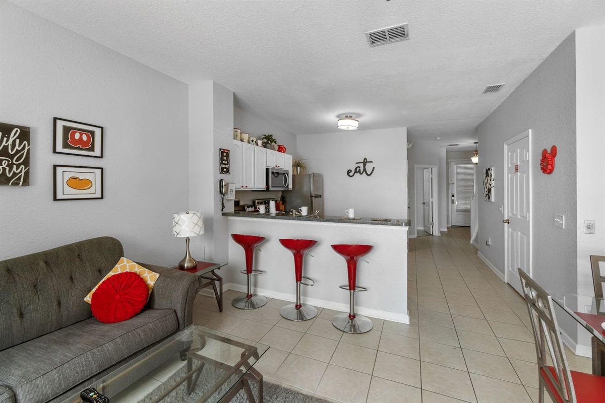 - Cozy living space with soft seating, glass coffee table, and bright accents  
- Kitchen features stainless steel appliances and plenty of counter space  
- Red bar stools add a fun pop of color for casual meals or conversation  