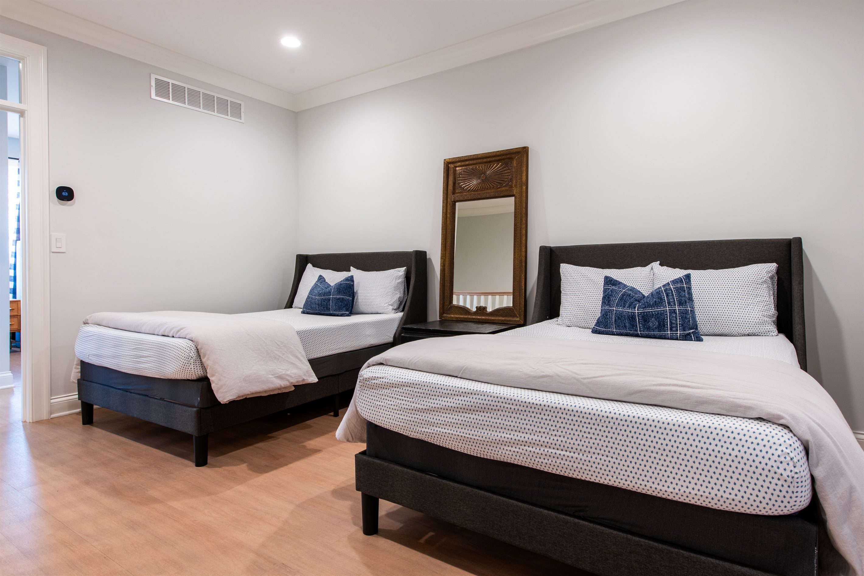 Loft/Additional sleep setup with two neatly made full beds, featuring modern black headboards and crisp bedding, accompanied by a decorative mirror adding depth to the room. Perfect for guests or siblings sharing a space.